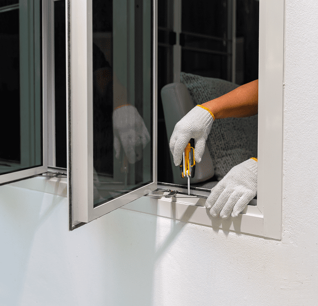 Gloved hands holding screwdriver at window